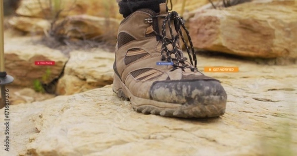 Fototapeta Resting brown hiking boot displaying mud-covered sole on sandstone boulder, with trekking pole