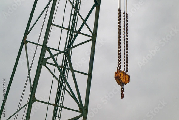 Fototapeta Green crane with large hook on yellow block hung by chains