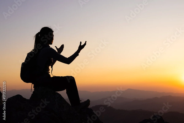 Fototapeta Silhouette of a women is praying to God on the mountain. Praying hands with faith in religion and belief in God on blessing background. Power of hope or love and devotion.