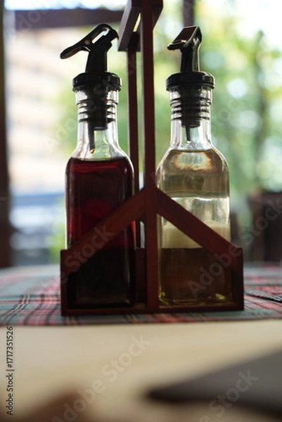 Fototapeta Bottles of olive oil and vinegar in wooden holder on restaurant table – close up of condiments set with glass bottles, seasoning, sauces for cooking, dining and gastronomy background