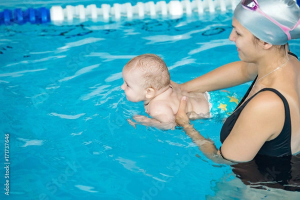 Fototapeta Young mother with her little son, attending swimming lessons for newborns, in public swimming pool