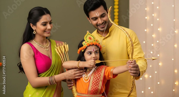 Fototapeta A child dressed as Lord Rama is supported parents elegant traditional attire while holding a bow and arrow