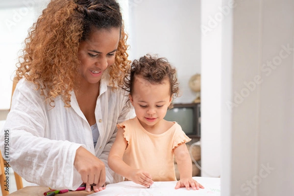 Fototapeta Enjoy happy smiling love family. Mother with little girl learning and writing in book with pencil making homework at home. Education concept	