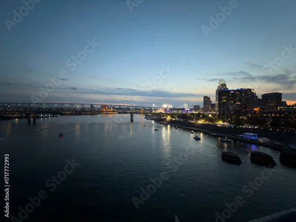 Fototapeta Evening panoramic view of Oktoberfest in Cincinnati, Ohio, with crowds gathered along the riverfront steps, illuminated tents, and boats floating on the Ohio River.