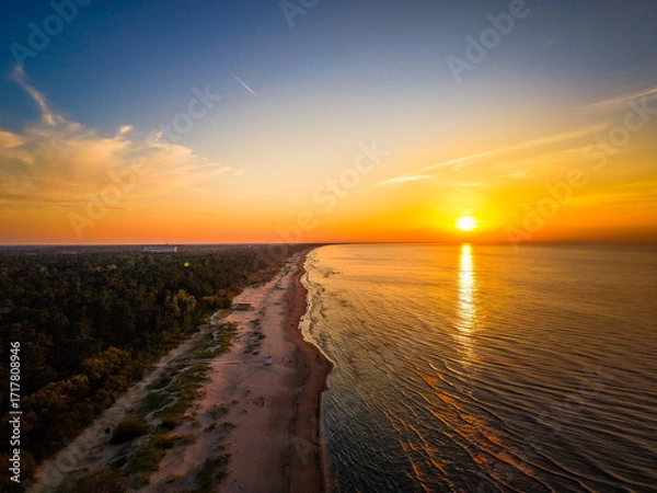 Fototapeta A breathtaking aerial view of a serene sunset over a sandy beach, with the sun casting golden hues across the sky and sea