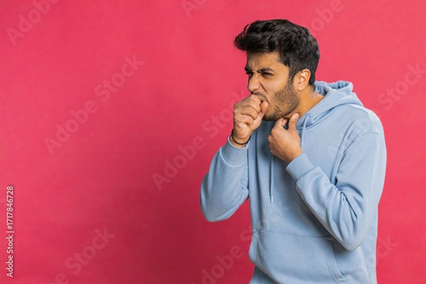 Fototapeta Unhealthy Indian young man coughing covering mouth with hand feeling sick, allergy or viral infection disease symptoms, infection, pain, virus. Hispanic Hindu guy isolated on red studio background