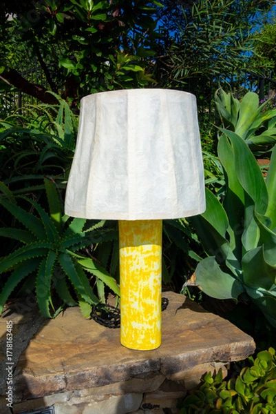 Fototapeta Yellow table lamp with paper lampshade set in front of some nice landscaping.