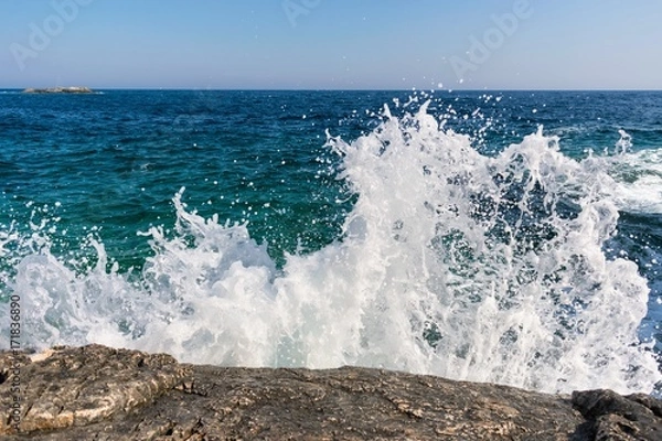 Fototapeta White wave splashing against rocky shore