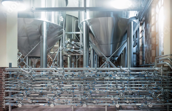 Fototapeta Fermentation tanks and complex pipeline system in modern beer brewery for industrial beverage production, alcohol processing, clean technology, automated food manufacturing, stainless equipment.