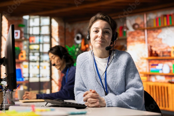 Fototapeta Portrait of smiling call center agent handling customer inquiries, complaints and support requests in office. Happy woman doing customer service job assisting customers with issues related to products