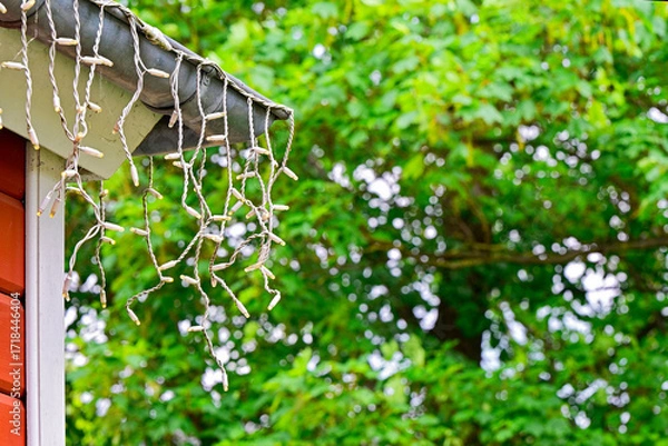 Fototapeta Roof corner with downspout and cascading warm string lights