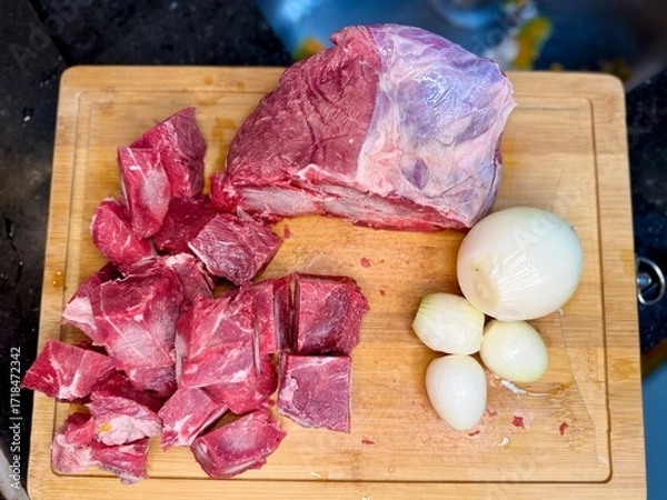 Fototapeta Carne em cubos cortas sobre a mesa com fundo desfocado e cebolas e panela con nivel de agua.