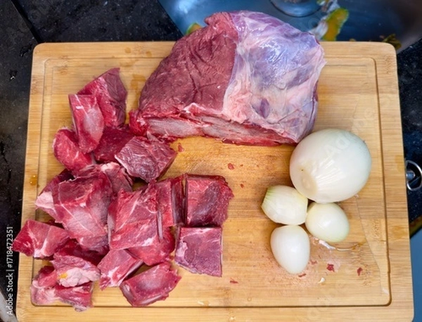 Fototapeta Carne em cubos cortas sobre a mesa com fundo desfocado e cebolas e panela con nivel de agua.