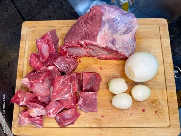 Fototapeta Carne em cubos cortas sobre a mesa com fundo desfocado e cebolas e panela con nivel de agua.