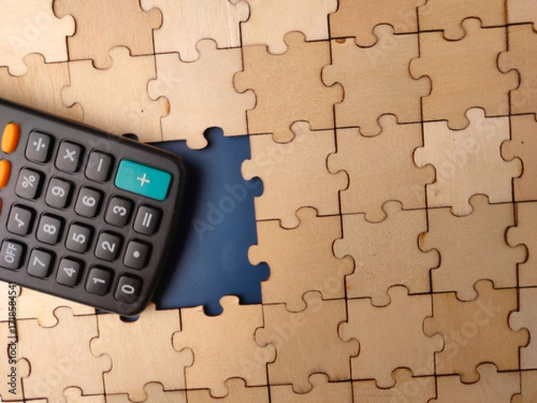 Fototapeta The image displays a calculator placed on a wooden jigsaw puzzle with a missing piece