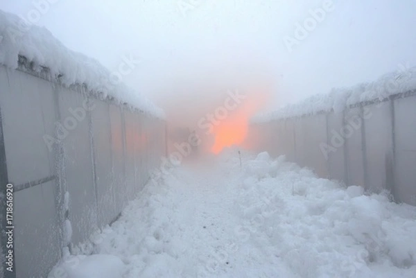 Fototapeta Snow-covered pathway between misty structures