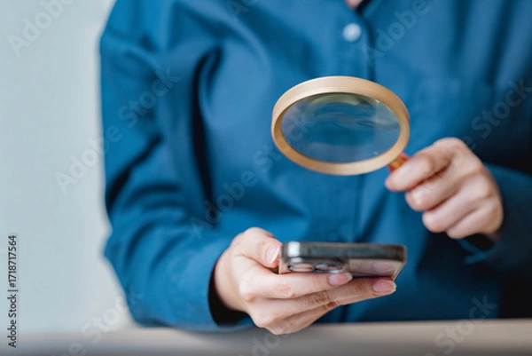 Obraz Close-up of a person using a magnifying glass to examine a smartphone, symbolizing digital analysis, online security, and modern technology research.