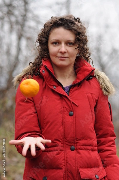 Fototapeta Curly girl in a red jacket tosses an orange
