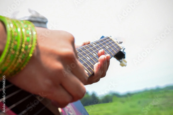 Fototapeta Close-Up of Hands Playing a Guitar Outdoors on a Sunny Day