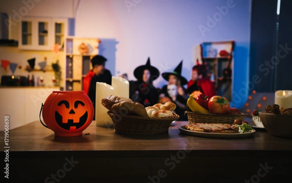 Fototapeta A cheerful group of friends dressed as witches and devils celebrate Halloween together,raising glasses of wine around a festive table with pumpkins,candles, bread,decorations in  cozy indoor setting