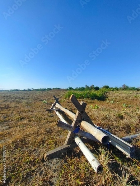 Obraz Low-angle view of metal pipe structure on dry grassy field under clear blue sky. Ideal for military, outdoor, rural, or environmental contrast-themed visual content