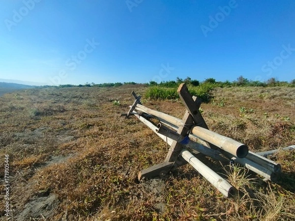 Fototapeta Low-angle view of metal pipe structure on dry grassy field under clear blue sky. Ideal for military, outdoor, rural, or environmental contrast-themed visual content