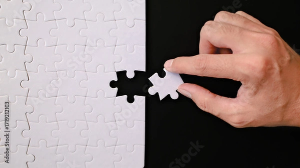 Fototapeta A hand connects puzzle pieces on a black background, completing a task or solving a problem