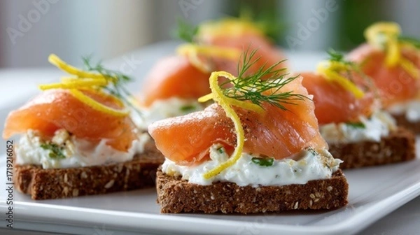 Fototapeta Close-up of several canap?s featuring smoked salmon atop a creamy spread on dark bread, garnished with lemon zest and dill