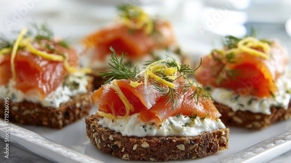 Fototapeta Four elegant canap?s featuring smoked salmon atop a creamy spread and whole-grain bread, garnished with dill and lemon zest