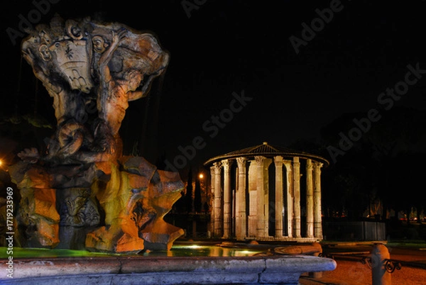 Fototapeta Temple of Hercules Victor ancient ruins and beautiful baroque Fountain of the Tritons lit up at night in Rome