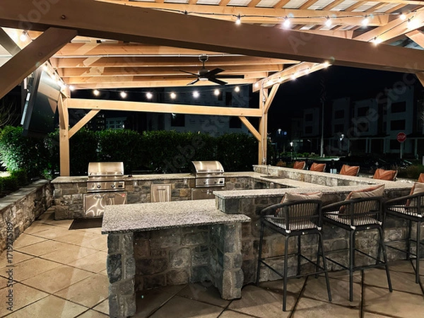Fototapeta Outdoor stone bar and grill area at night with string lights and seating