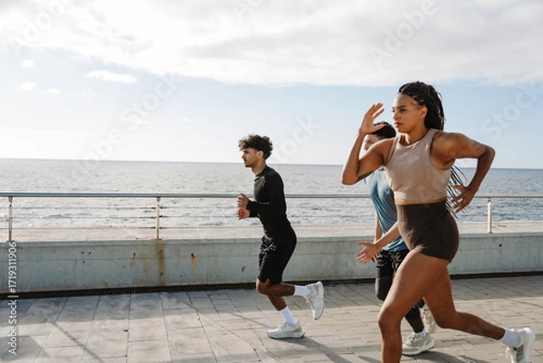 Fototapeta A group of three athletes running on a sidewalk by the sea