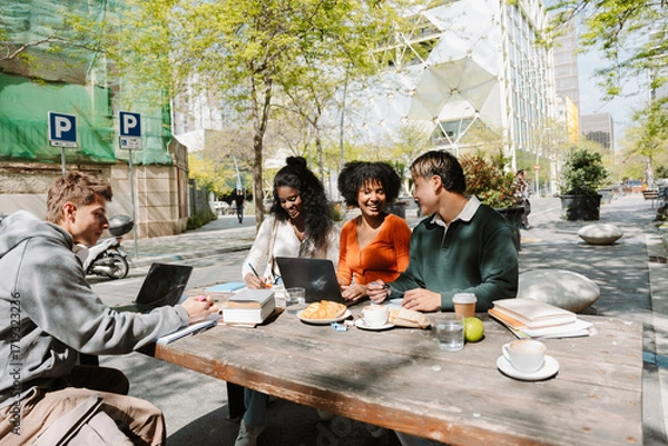 Fototapeta A group of four students are sitting at a table and laughing during lunch
