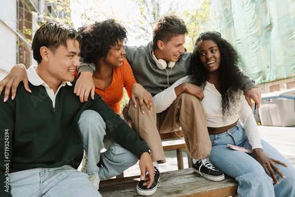 Fototapeta A group of four students sit at a table and laugh while one of them talks
