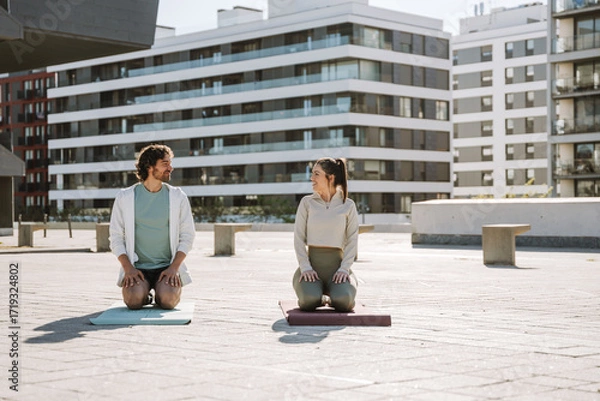 Fototapeta Male and female athletes sitting on mats and smiling while looking at each other