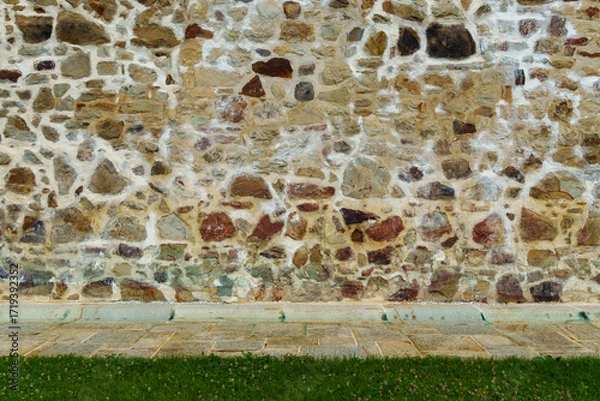 Fototapeta old stone wall of ancient monastery and green grass lawn as abstract background