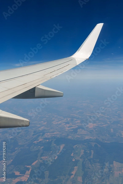 Fototapeta view from airplane window on wing and landscape below, horizon above planet and air haze, airplane view