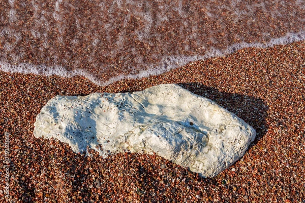 Fototapeta big beautiful white stone lies on coastline and small stones of beach of Adriatic Sea, with beautiful foaming wave, as abstract background of summer travel and vacation