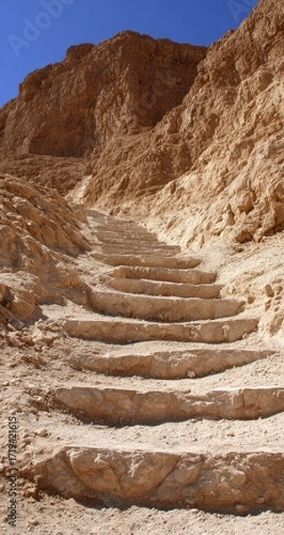 Fototapeta Ancient stone steps ascend a rugged desert canyon under a clear blue sky.