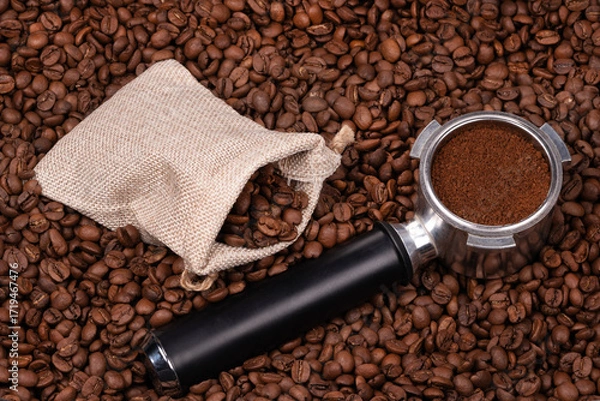 Fototapeta Jute bag and holder with ground coffee on the background of roasted coffee beans. coffee beans background texture.