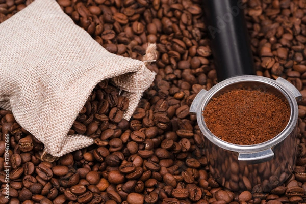 Fototapeta Jute bag and holder with ground coffee on the background of roasted coffee beans. coffee beans background texture.