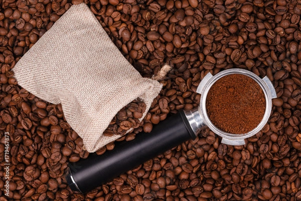 Fototapeta Jute bag and holder with ground coffee on the background of roasted coffee beans. coffee beans background texture.
