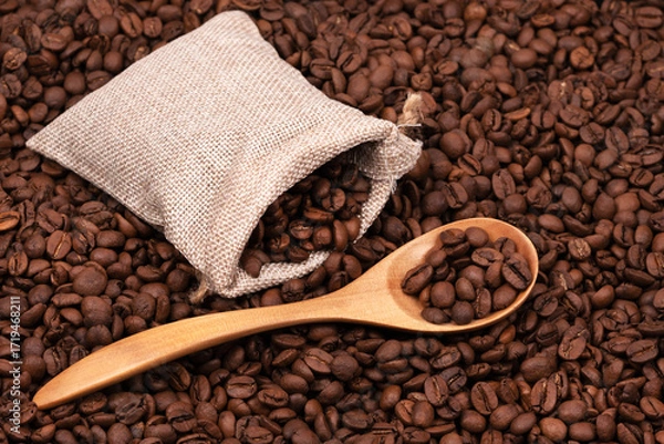 Fototapeta Jute bag with coffee beans and wooden spoon on the background of roasted coffee beans. coffee beans background texture.