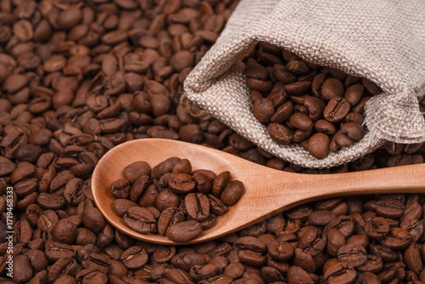 Fototapeta Jute bag with coffee beans and wooden spoon on the background of roasted coffee beans. coffee beans background texture.