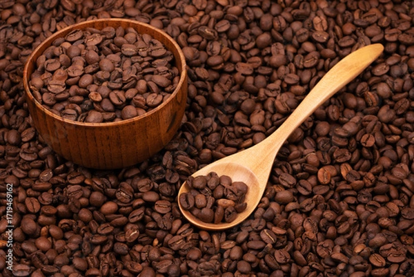 Fototapeta Wooden cup with coffee beans and wooden spoon on the background of roasted coffee beans. coffee beans background texture close up top view