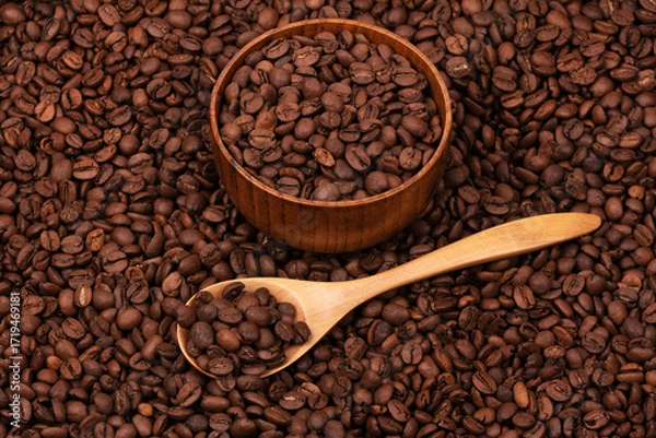 Fototapeta Wooden cup with coffee beans and wooden spoon on the background of roasted coffee beans. coffee beans background texture close up top view