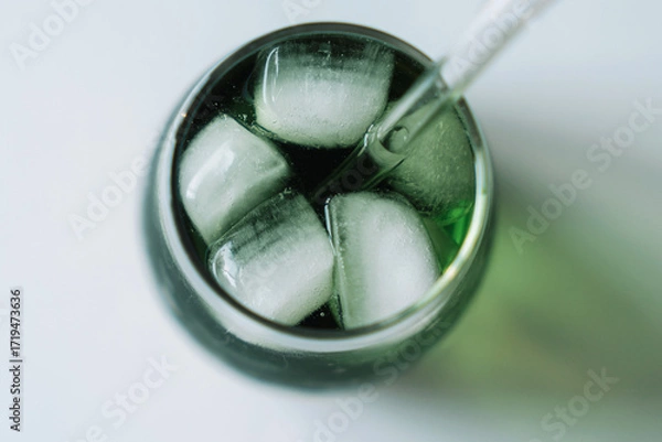 Fototapeta Macro top view: ice cubes in a green chlorophyll drink with a glass straw. Texture and freshness. Horizontal macro.