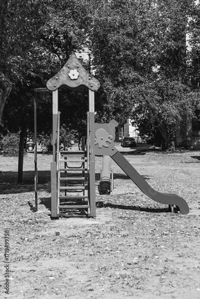 Fototapeta A black and white photo of a playground slide evokes a sense of quiet nostalgia. The play equipment stands still under the midday sun, highlighting its intricate structure and peaceful solitude.

