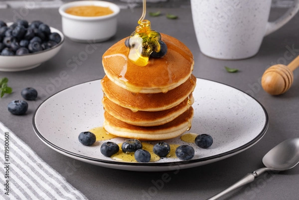 Fototapeta A stack of pancakes is drizzled with honey. Blueberries are placed next to the pancakes