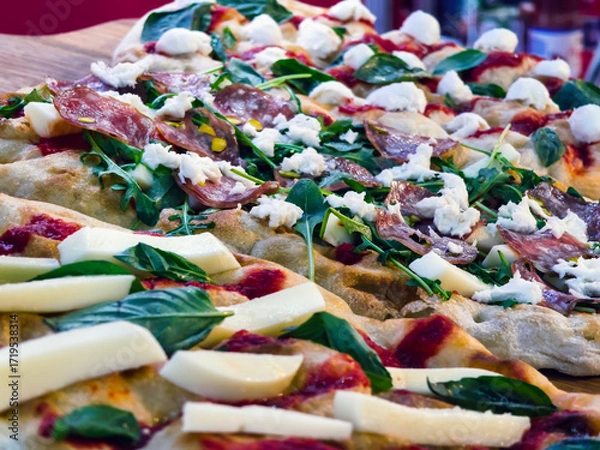 Fototapeta Delicious fresh pizza topped with salami, spinach, and cheese served at a bustling restaurant in the afternoon